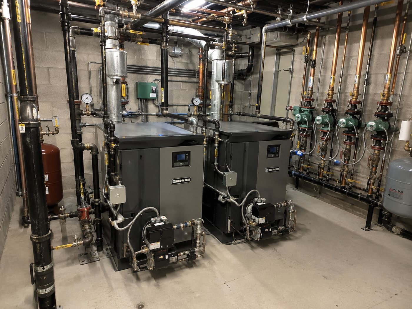 A mechanical room with two gas boilers, circulator pumps, expansion tanks and labelled distribution piping